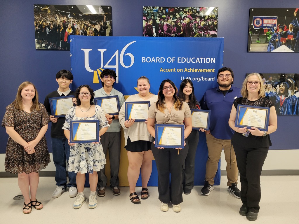 A group of people stands in a room, holding certificates. A blue banner with white text is behind them.