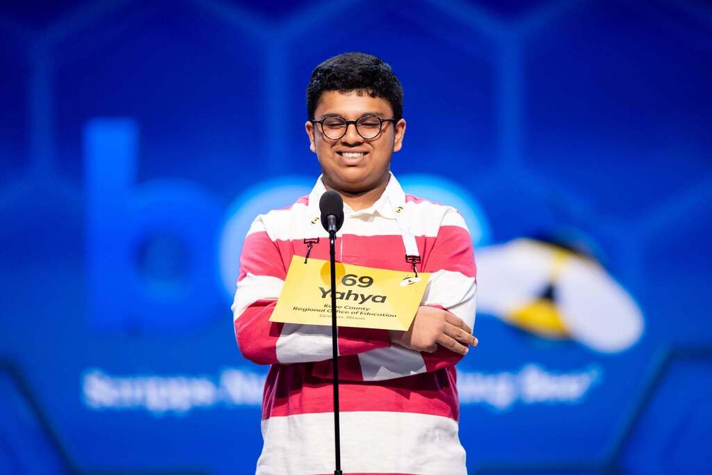 A person wearing glasses and a striped shirt stands at a podium with a microphone.