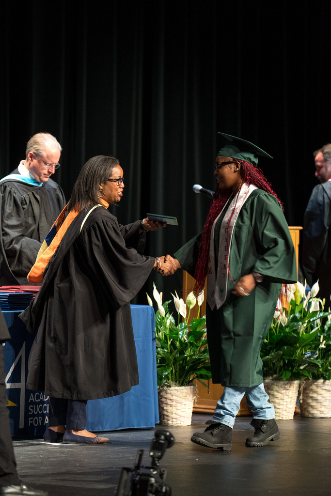 A woman hands a high school student a diploma on stage