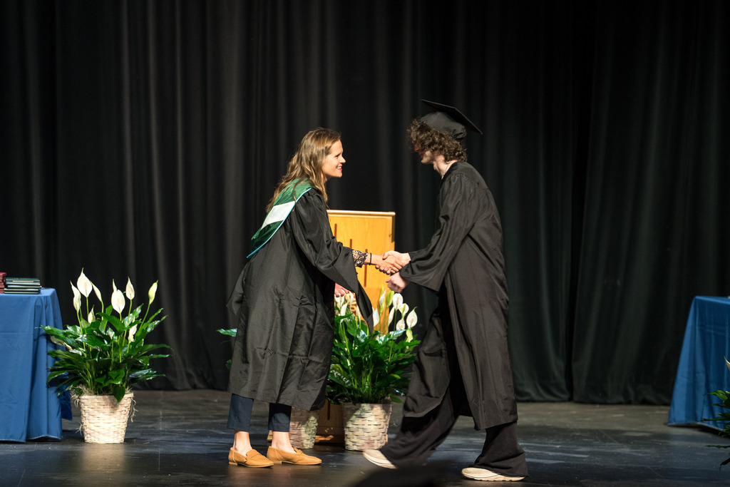 A woman hands a high school student a diploma on stage