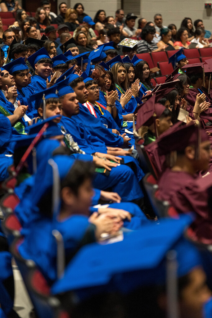 A group of high school students sit in caps and gowns in an auditorium