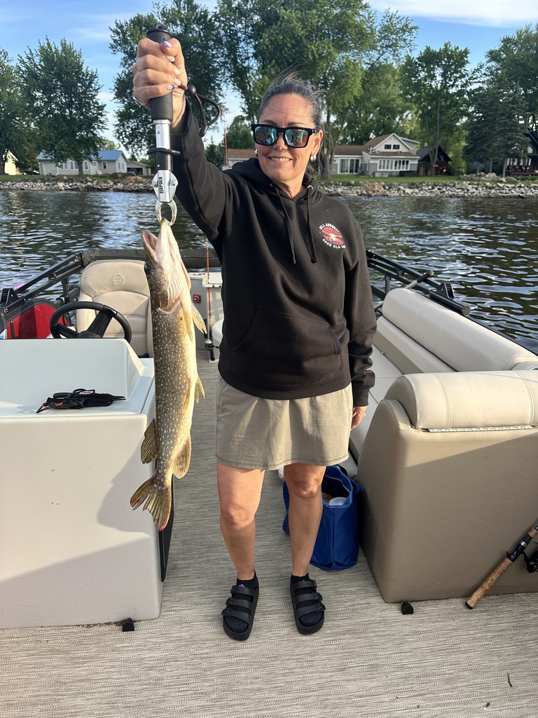 A person holding a fish up while standing on a boat with beige seats and a blue bag.