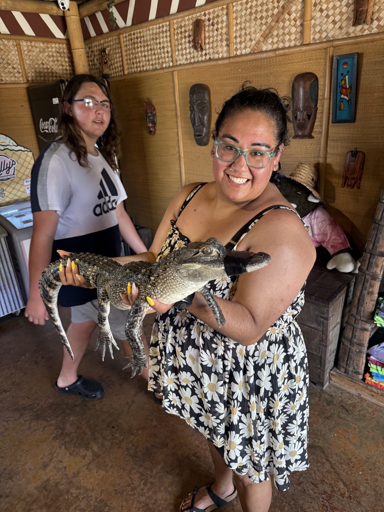 Two women inside a building, one holding a small alligator, the other standing next to her.