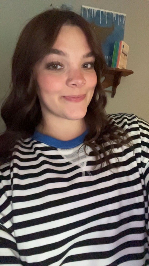 A woman with brown hair smiles at the camera. She wears a striped shirt with blue on the collar.