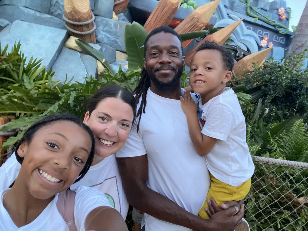 Four people smile in front of a jungle-themed park background. A man holds a boy on his lap.