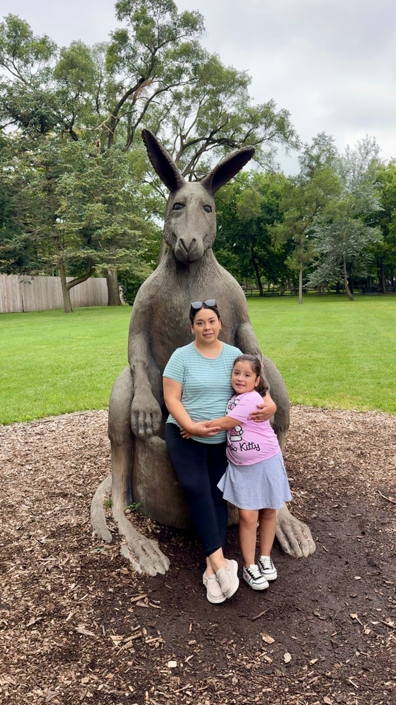Woman and child standing in front of a large kangaroo statue in a grassy park.