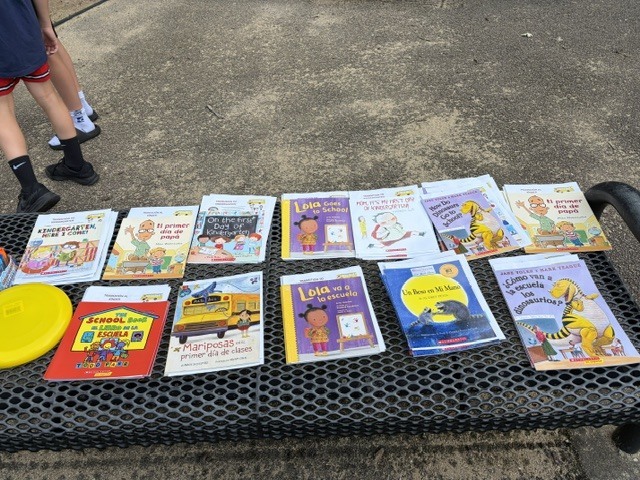 A black bench with children's books and a yellow frisbee on it. The bench is outdoors.
