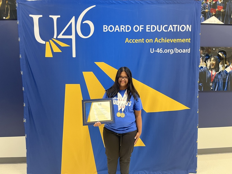 Student Devkee Patel stands in front of Accent on Achievement backdrop, holding her award