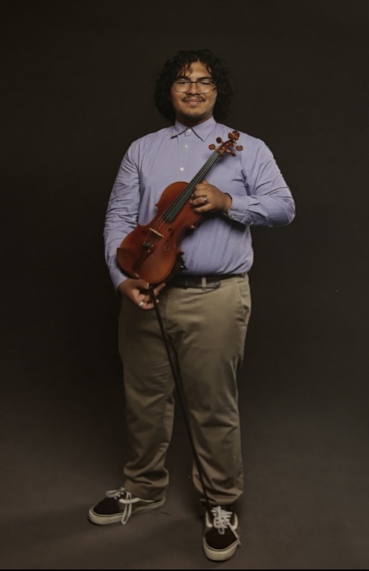 A young man holds a  violin in front of him while smiling