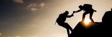 (silhouette of one person helping another pulling him up a mountain)