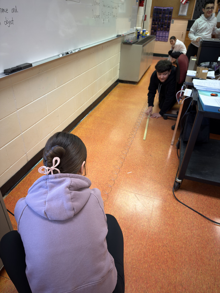 Students in Mrs. Ramos’ class use slinkies to explore waves, stretching and observing them while the teacher guides the hands-on experiment.