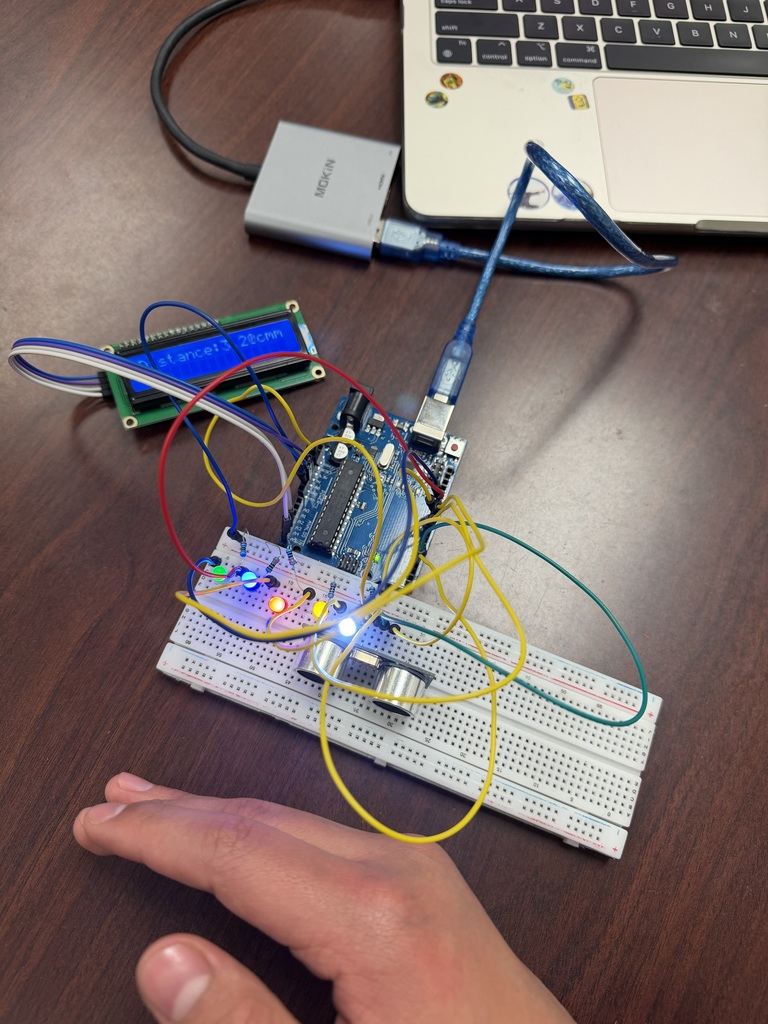 An Arduino microcontroller project is set up on a breadboard with an LCD display, LEDs, and an ultrasonic sensor. A hand is positioned near the sensor, and the LCD shows