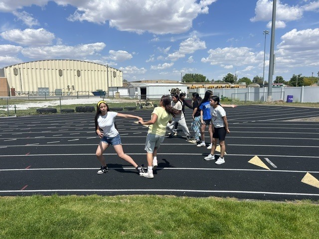 A group of girls are practicing a relay race on a running track. They are passing a baton between each other.