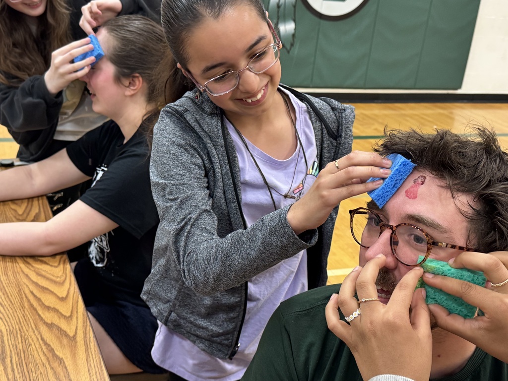 A group of young people are playfully applying temporary tattoos to their teachers' faces using sponges.
