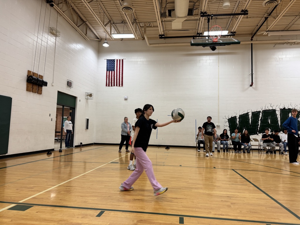 student serving the volleyball during staff vs. student volleyball game