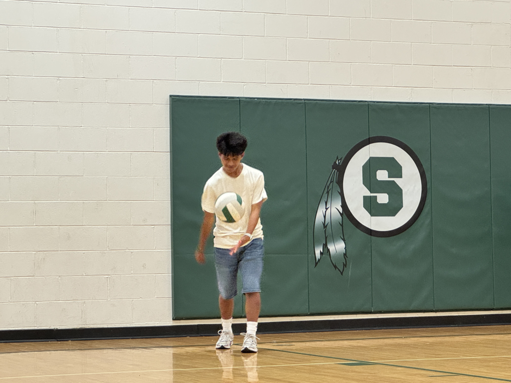 student serving the volleyball during staff vs. student volleyball game