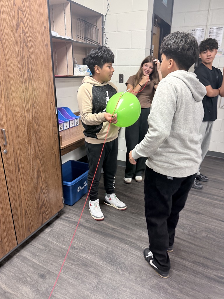 Students are working together on a hands-on balloon activity, demonstrating teamwork, communication, and problem-solving.
