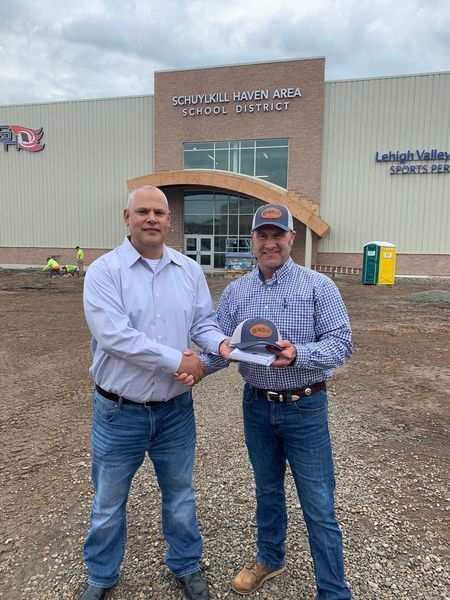 closer up show of two men shaking hands with one man passing a hat to the other person