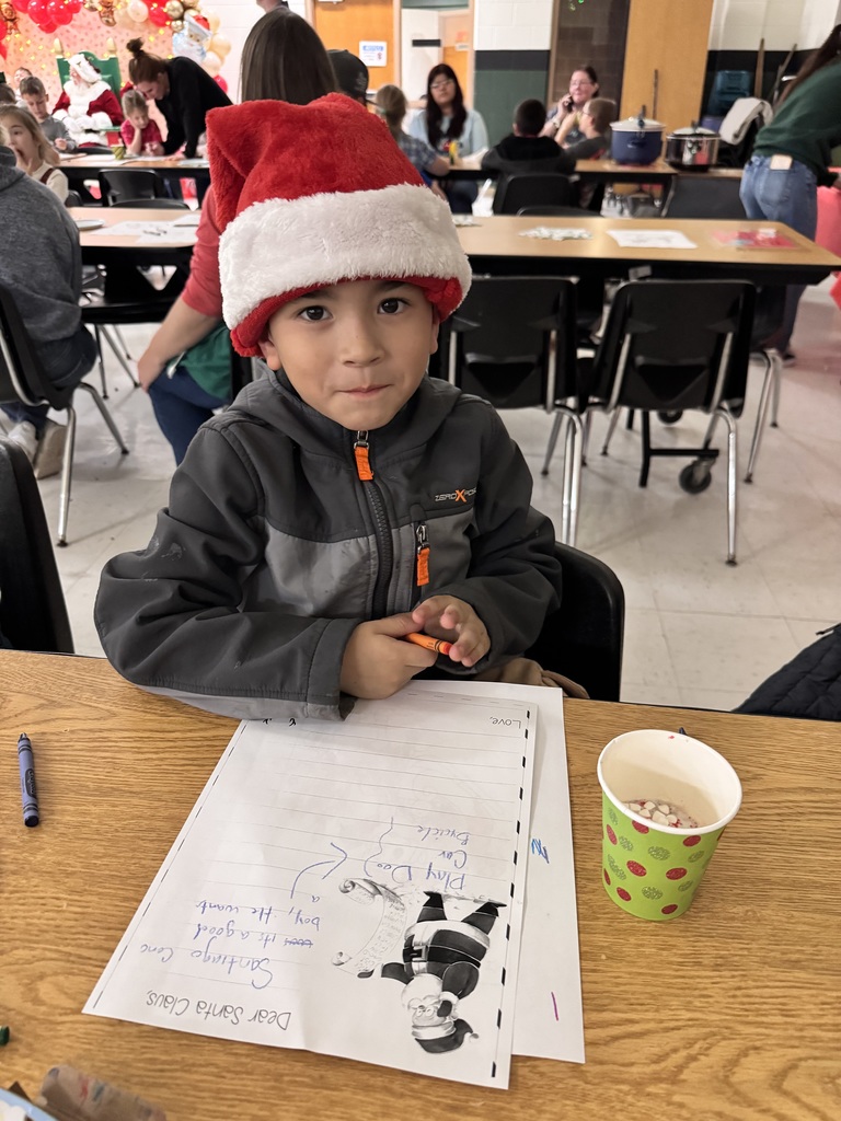 young boy in a grey jacket with a santa hat writing a letter to Santa