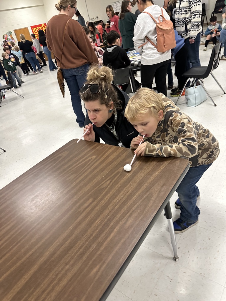 adult woman and child playing a game of blowing a cotton ball across the table with a straw