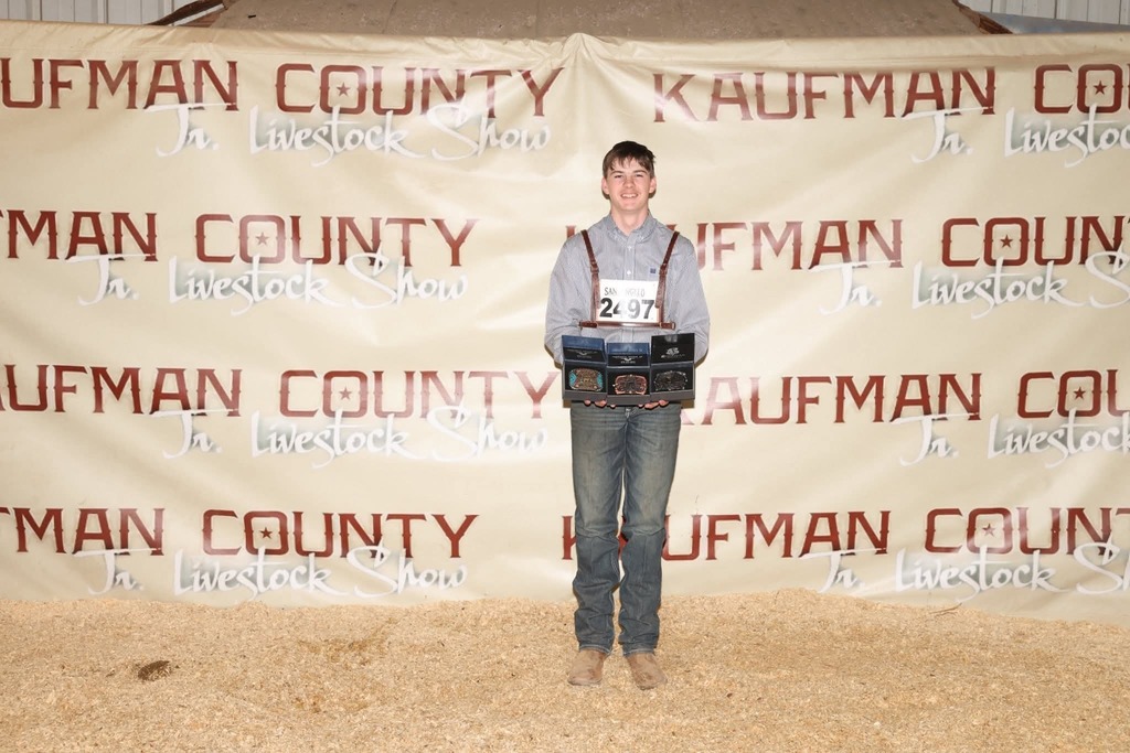 male student holding three buckles that he was awarded
