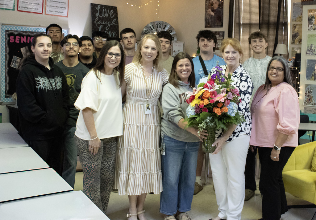 group photo of a teacher and four members of listing smiling at the camera with students in the picture