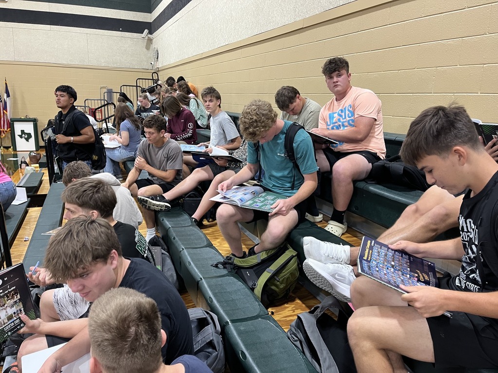 group of students sitting in the gym stands signing yearbooks