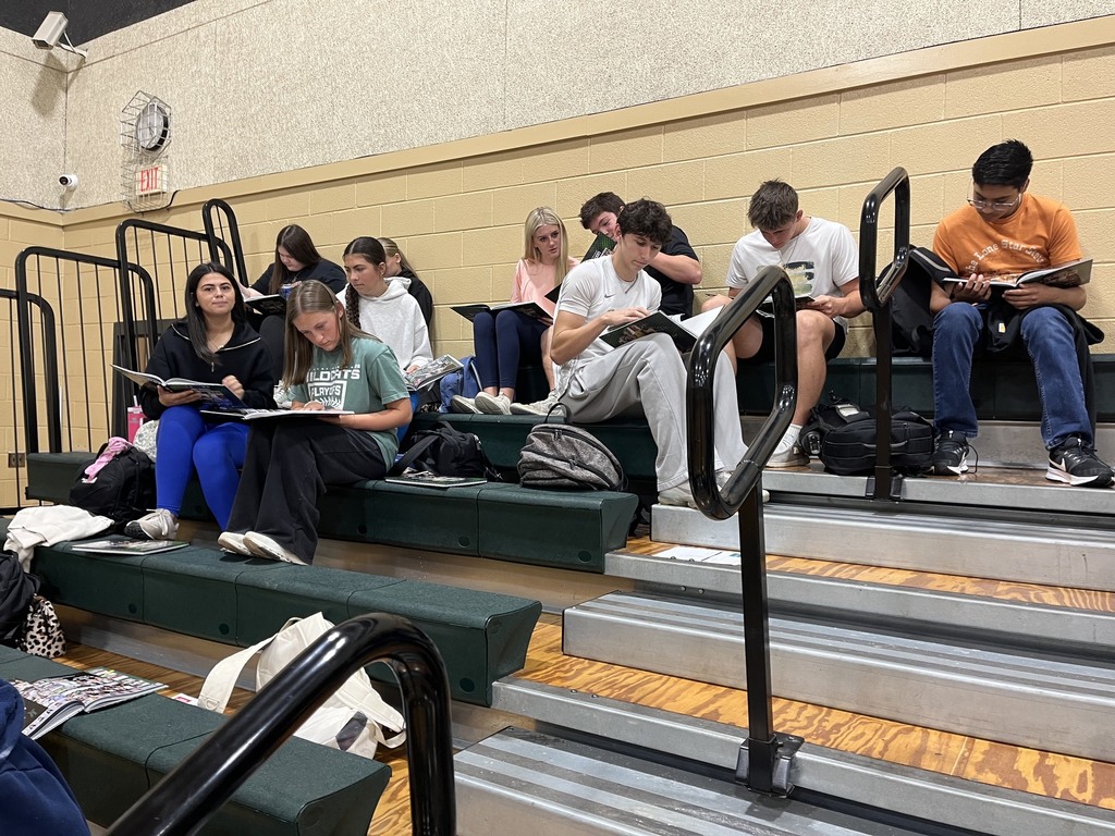 group pf students sitting in the gym bleachers signing yearbooks