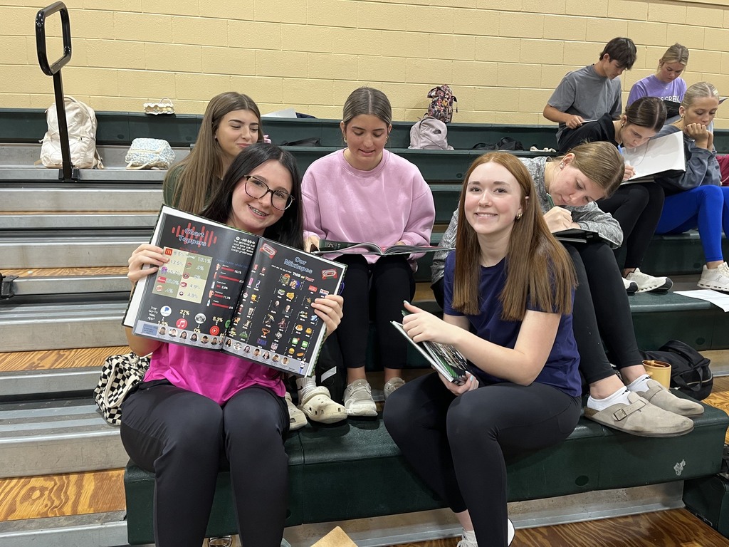 group of five female students looking at their yearbooks with one of them showing the inside of her yearbook to the camera