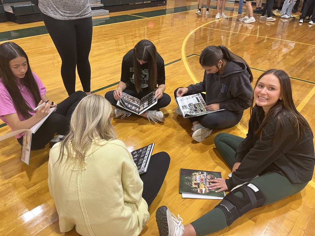 group of five students sitting on the gym floor looking at yearbooks