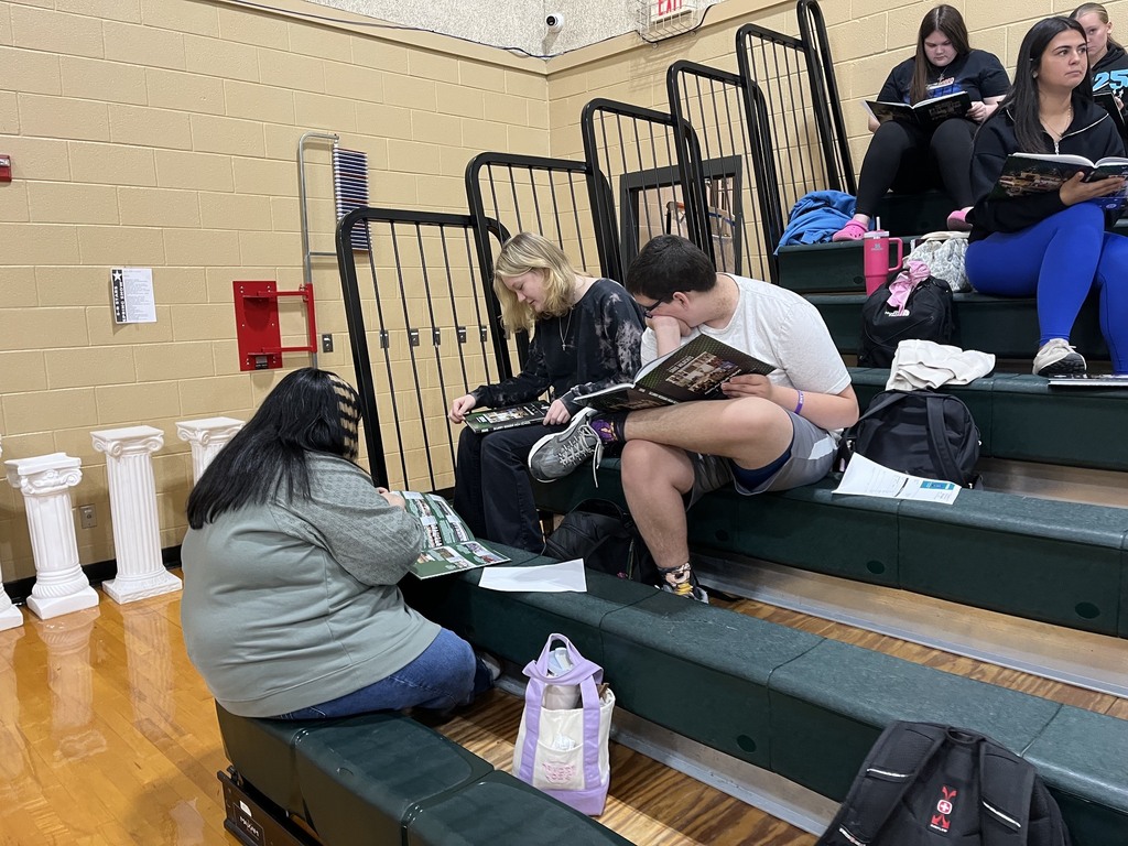 three students sitting the in gym bleachers looking at their yearbooks