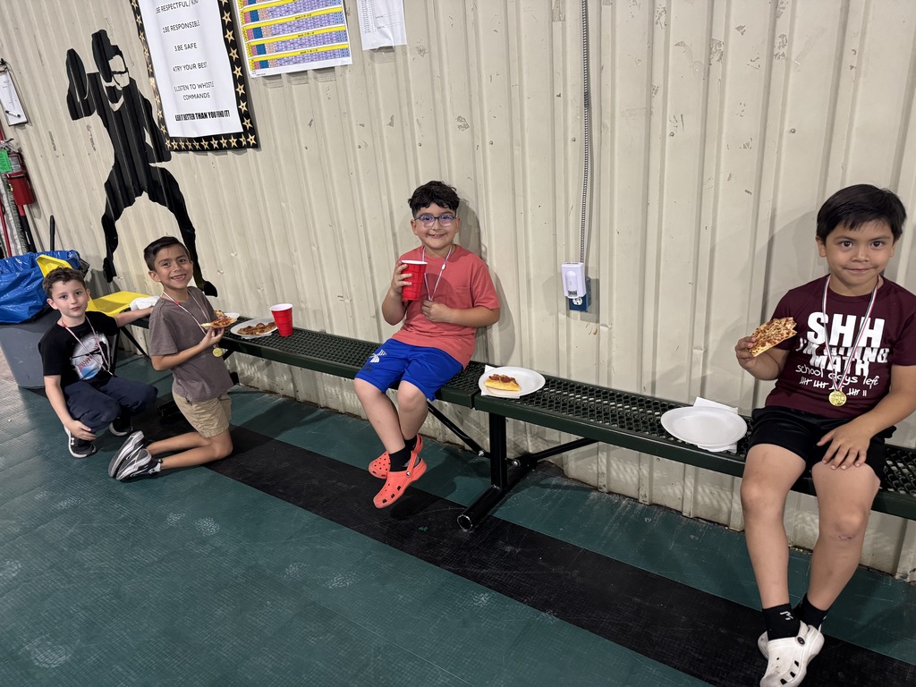 four male students eating their pizza my the metal bench