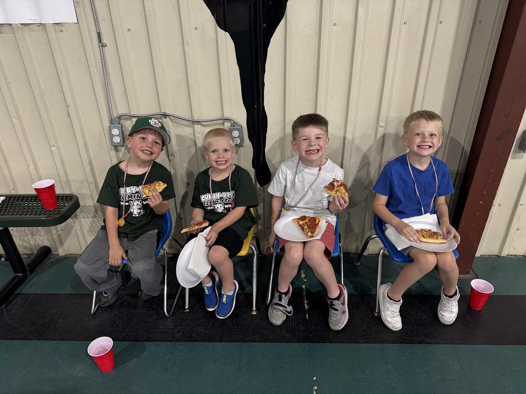 group of four male students sitting in blue chairs eating pizza while smiling for the camera