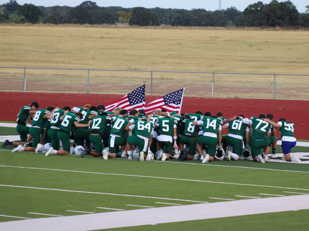 varsity scurry-rosser football team kneeling to prayer next to american flags
