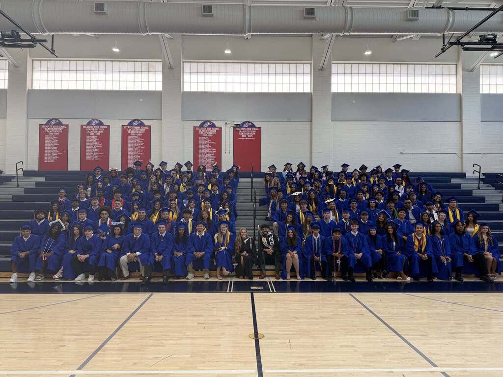 A group of students wearing blue robes pose for a photo on a sports court.