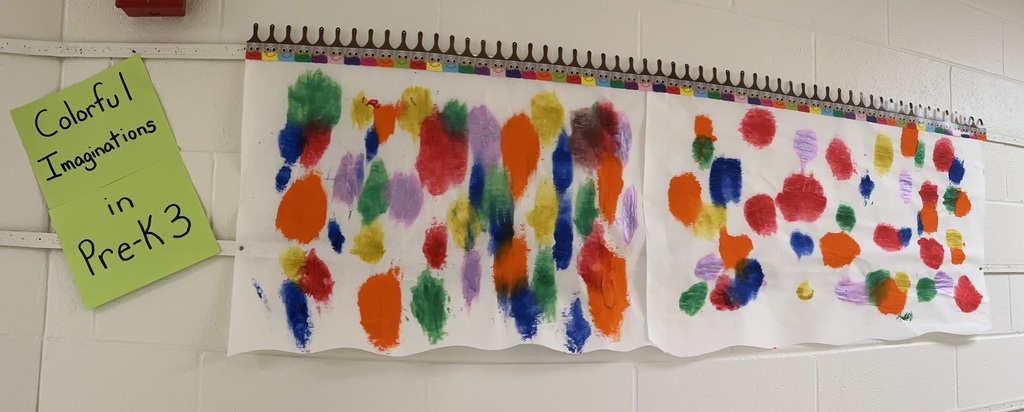 A white wall displays a colorful art project. It features vibrant, circular shapes in various colors. A note reads "Colorful Imaginations in PreK3".