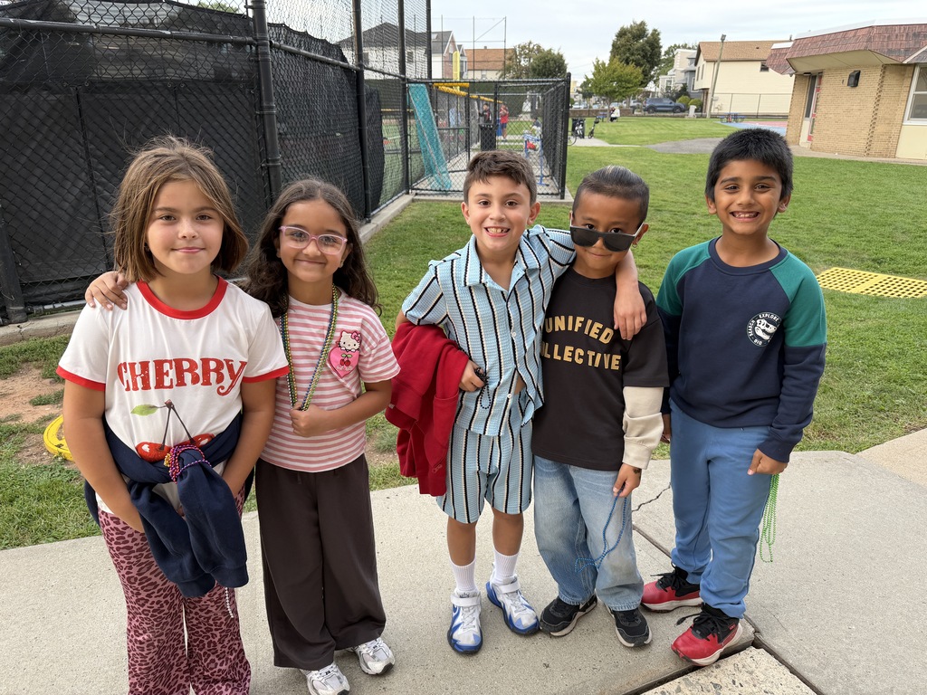 Five children standing together on a sidewalk, some wearing glasses, near a fence and grass.