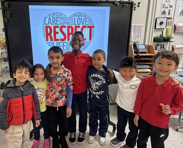 Seven children stand together in front of a screen displaying the word "Respect" with a heart around it.