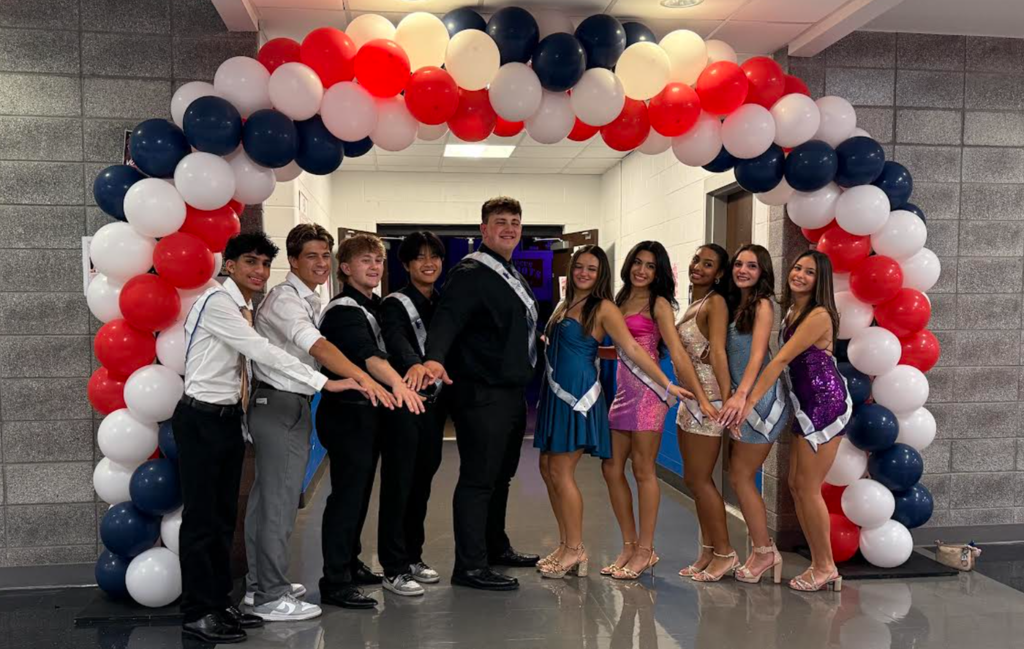 A group of people standing under a balloon arch, with colors red, white, and blue.