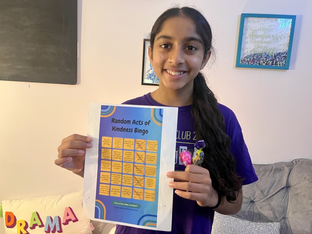 A girl holds up a sheet of paper with a bingo card on it in a room.