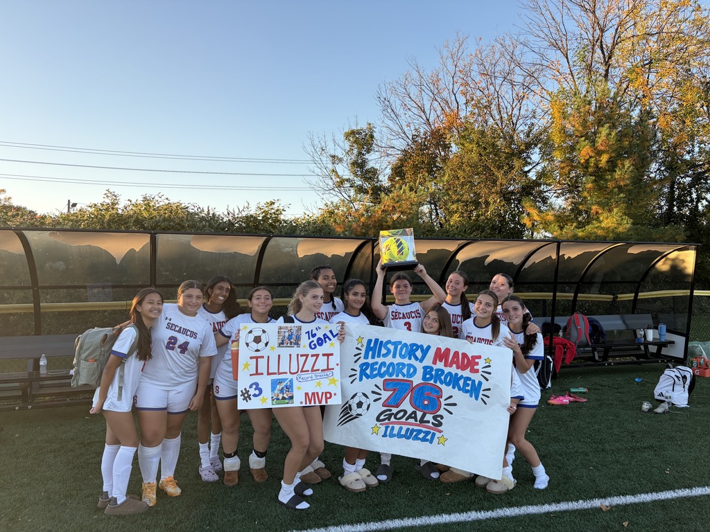 A group of women wearing soccer uniforms holding signs reading "History Made" and "78 Goals" on a field.