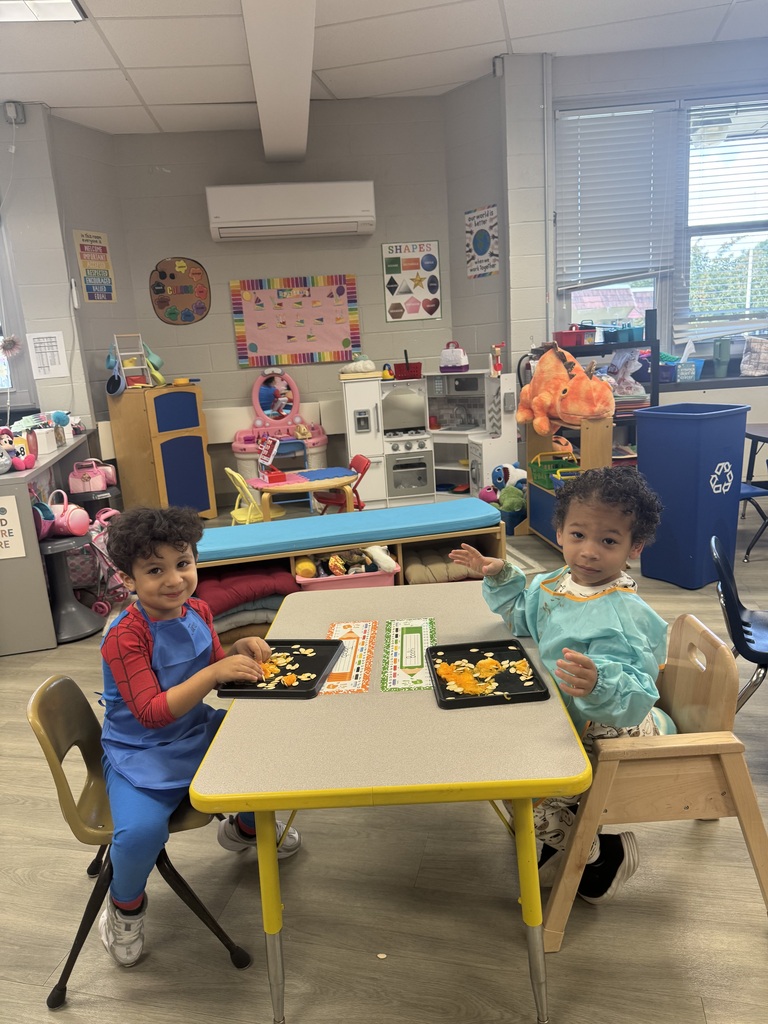Two young children sitting at a table with plates of food. Brightly lit room with colorful decor.