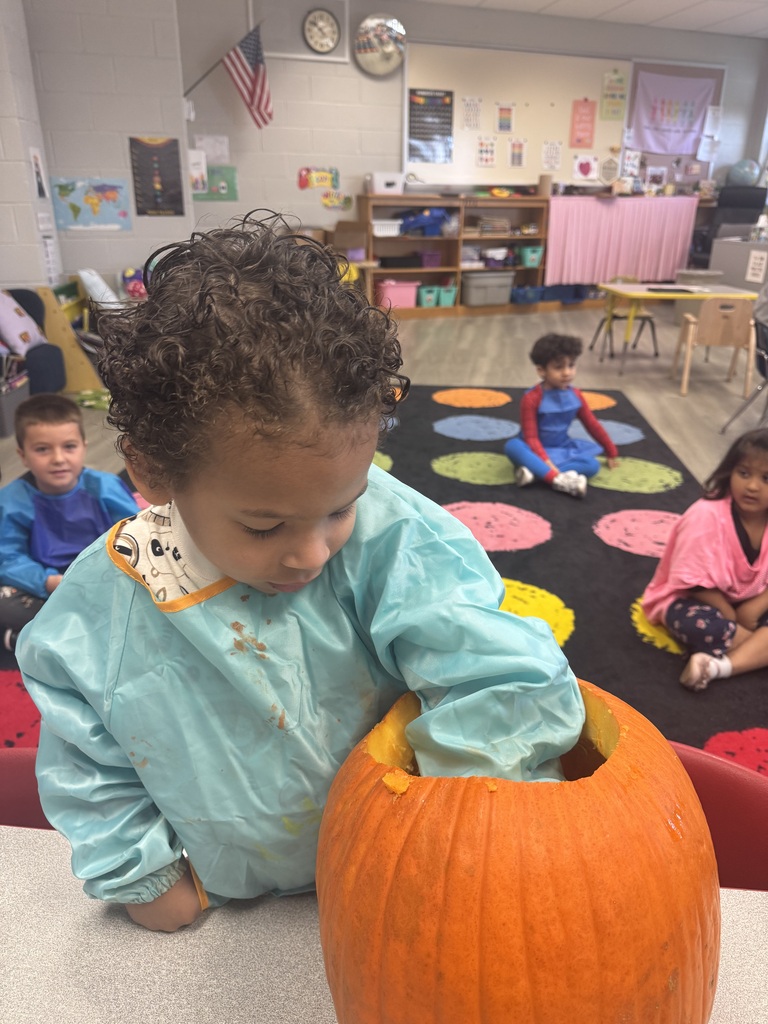 Child with curly hair scooping out seeds from pumpkin on a table. Children sitting on floor.