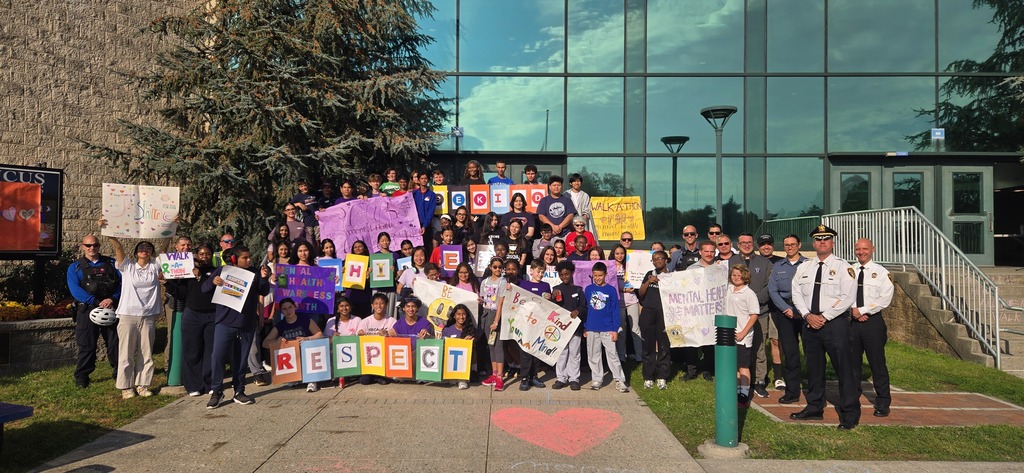 Many students and adults stand on a sidewalk holding signs. Some signs have the word "Respect" on them.