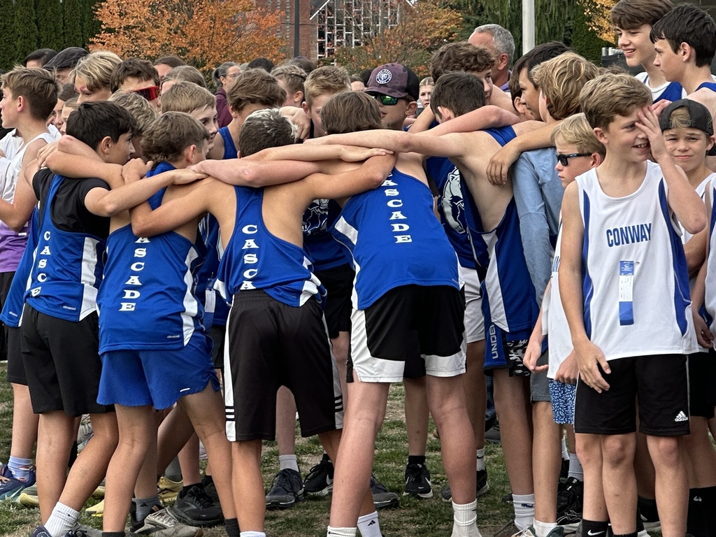 A group of 7th grade boys from the Cascade Middle School cross country team stands together at the starting line before their race, smiling and showing their team spirit.