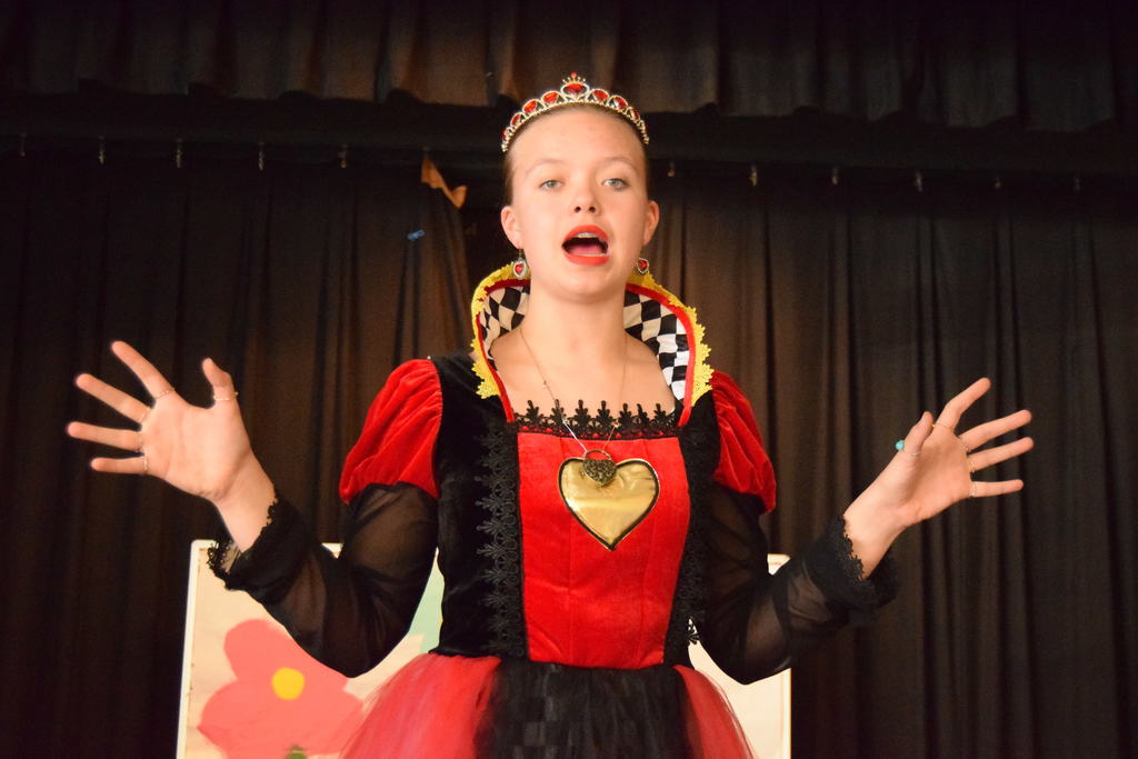 Cascade Middle School drama students in costume rehearsing for “Dorothy in Wonderland,” with characters from The Wizard of Oz and Alice in Wonderland gathered on stage under colorful lights.