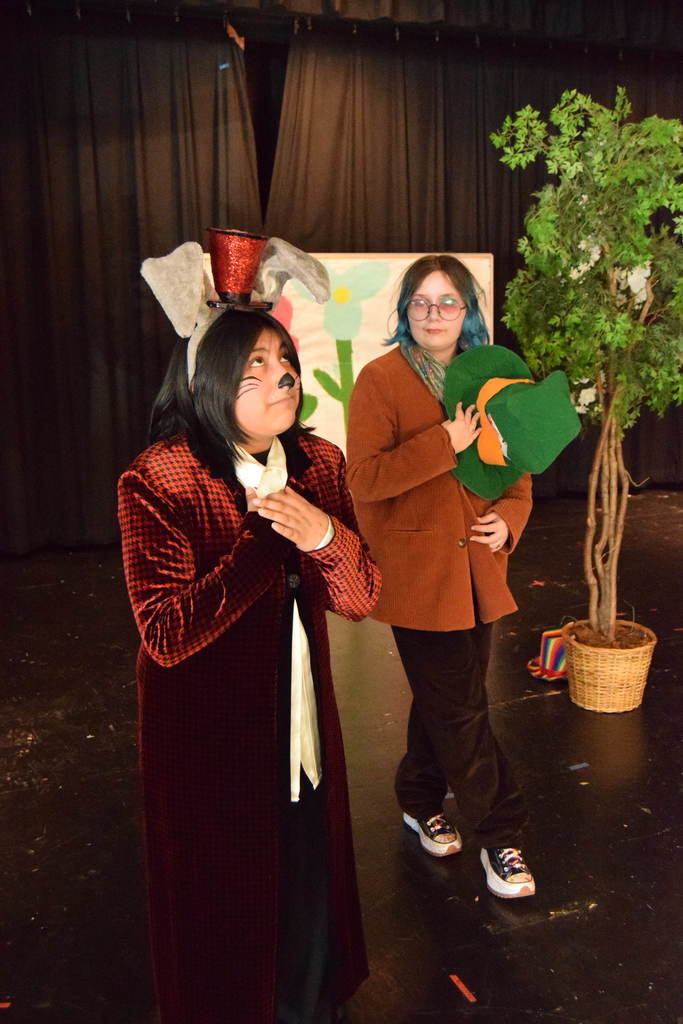 Cascade Middle School drama students in costume rehearsing for “Dorothy in Wonderland,” with characters from The Wizard of Oz and Alice in Wonderland gathered on stage under colorful lights.