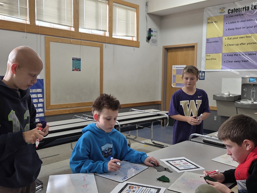 Students gather around a table at Big Lake Elementary, smiling as they work together on a math problem during the first Math Olympiad meeting.
