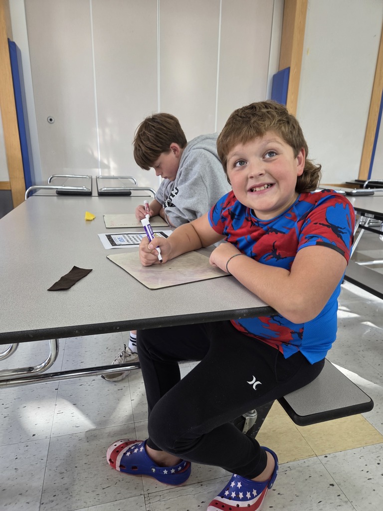 Students gather around a table at Big Lake Elementary, smiling as they work together on a math problem during the first Math Olympiad meeting.
