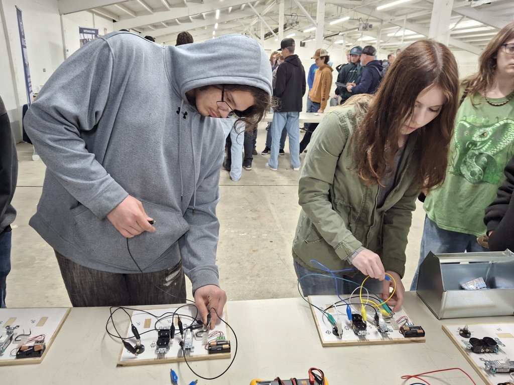 Students gather around an electrical panel display while learning about apprenticeship opportunities from JATC Electrician Apprenticeship representatives.